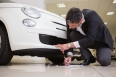 Man looking at the bumper while writing on clipboard at new car showroom