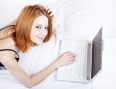 Beautiful red-haired girl with notebook in the bed.